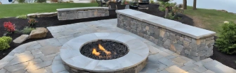 Stone veneer gas fire pit with a circular design, surrounded by outdoor seating in a cozy patio setting